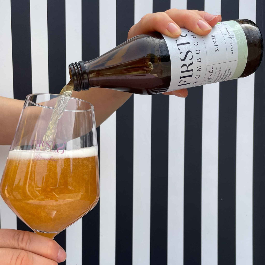 Kombucha wird aus Glasflasche in Glas eingeschenkt