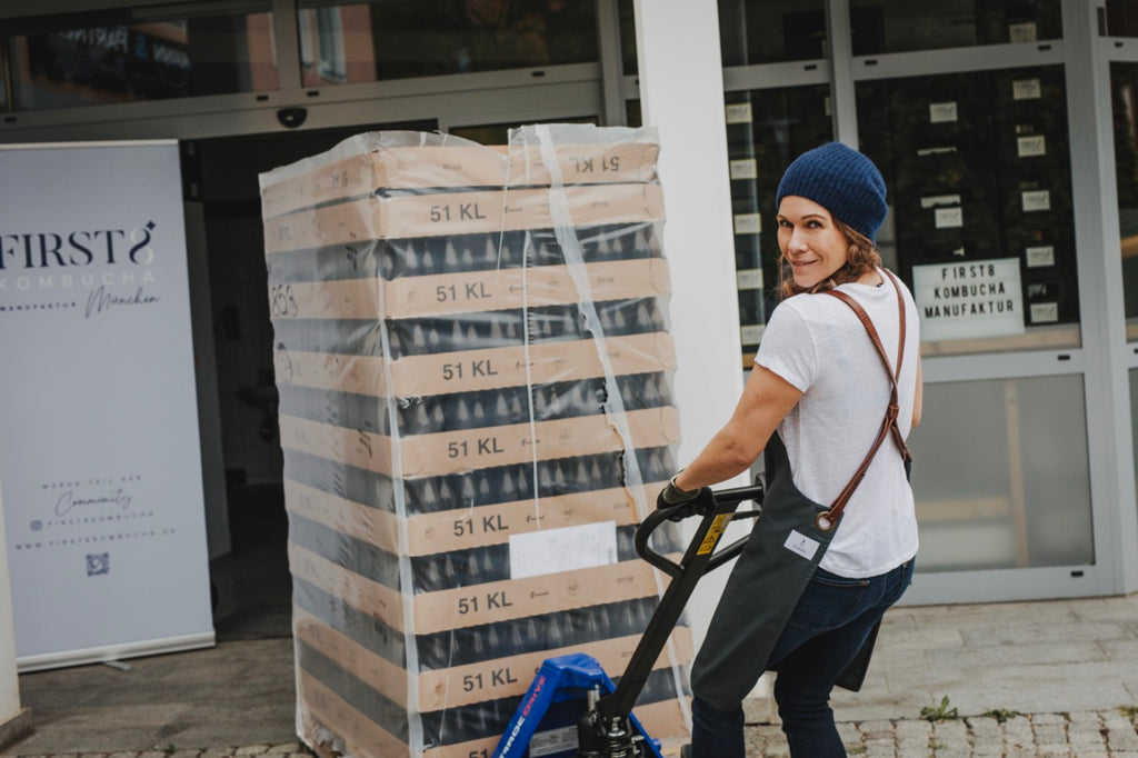 Arbeiten in der FIRST8 Kombucha brauerei - Brauerin zieht Palette mit Flaschen auf einem Hubwagen